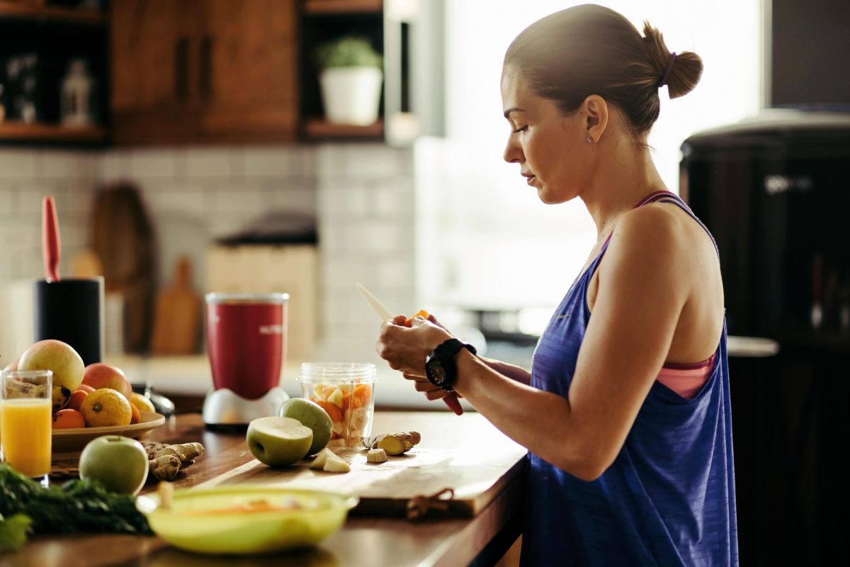 young-sportswoman-making-herself-healthy-smoothie-slicing-fresh-fruit-kitchen-min